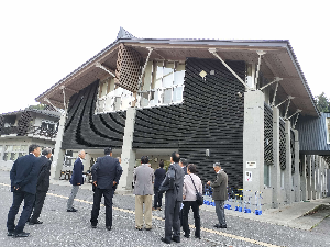 黒い壁をした建物を見上げるスーツの人たちの写真