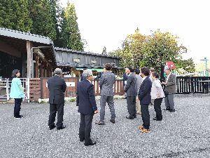 柵の向こうの建物を見るスーツの人たちの写真