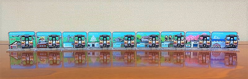 駅名と風景が描かれた11枚の列車型プレートが横一列に並んでいる写真