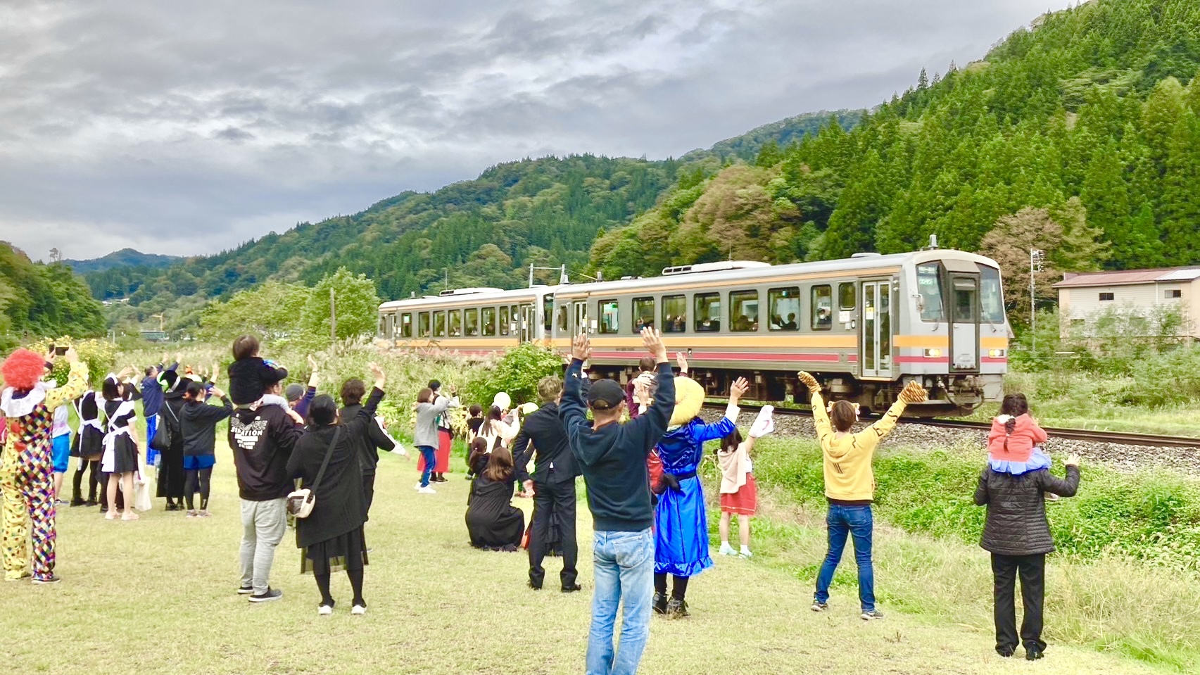 山のふもとを走る列車に老若男女が手を振っている写真
