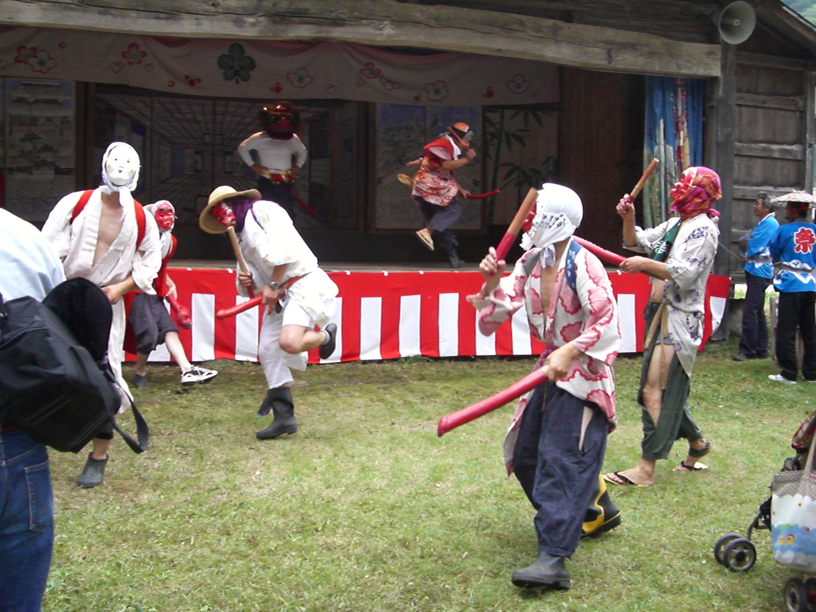 お祭りでお面を被った人たちがバチを持って踊っている写真