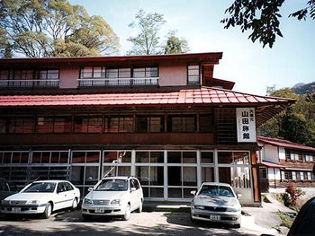 小谷温泉の老舗旅館山田旅館本館の写真。建物の前に車が数台停まっている。