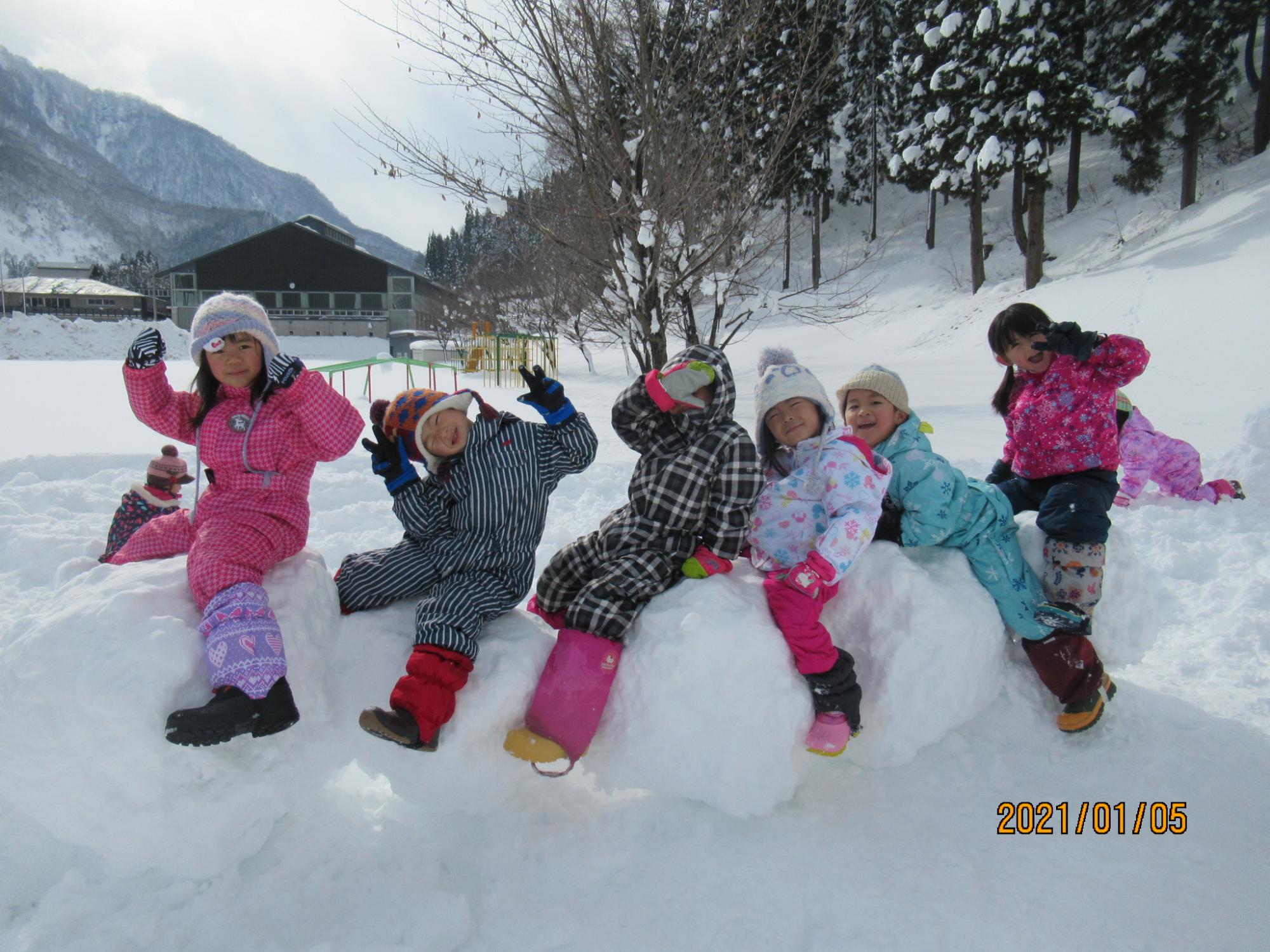 並んだ雪玉にまたがる園児達の写真