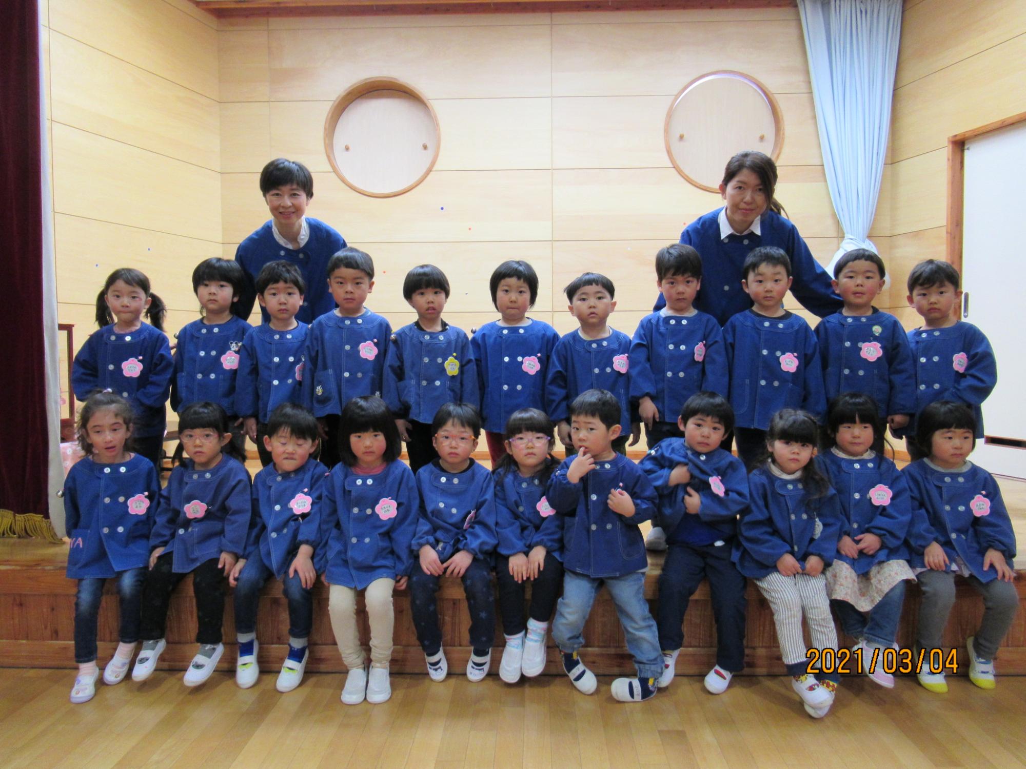 青い服の子供たちが室内で前を向いて2列になっている写真