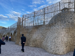 網目状の凸凹した高い壁を眺めている人たちの写真