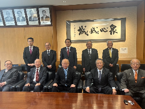 机の前に2列で並ぶスーツの男性達の記念写真