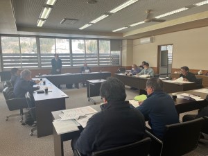 男性の話を机に座って聞く人たちの写真