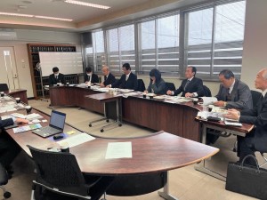 コの字型に並べられた机に着席して話し合うスーツの人達の写真