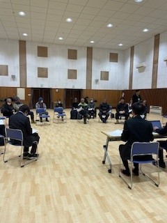 広いホールで椅子を円形に並べて人々が座っている写真